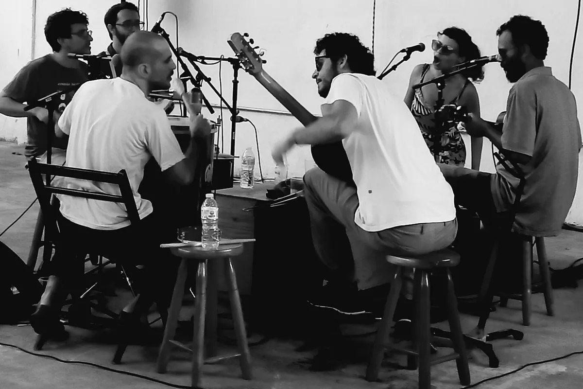 Zwart-witfoto van muzikanten met gitaren en microfoons op krukken bij een roda de samba