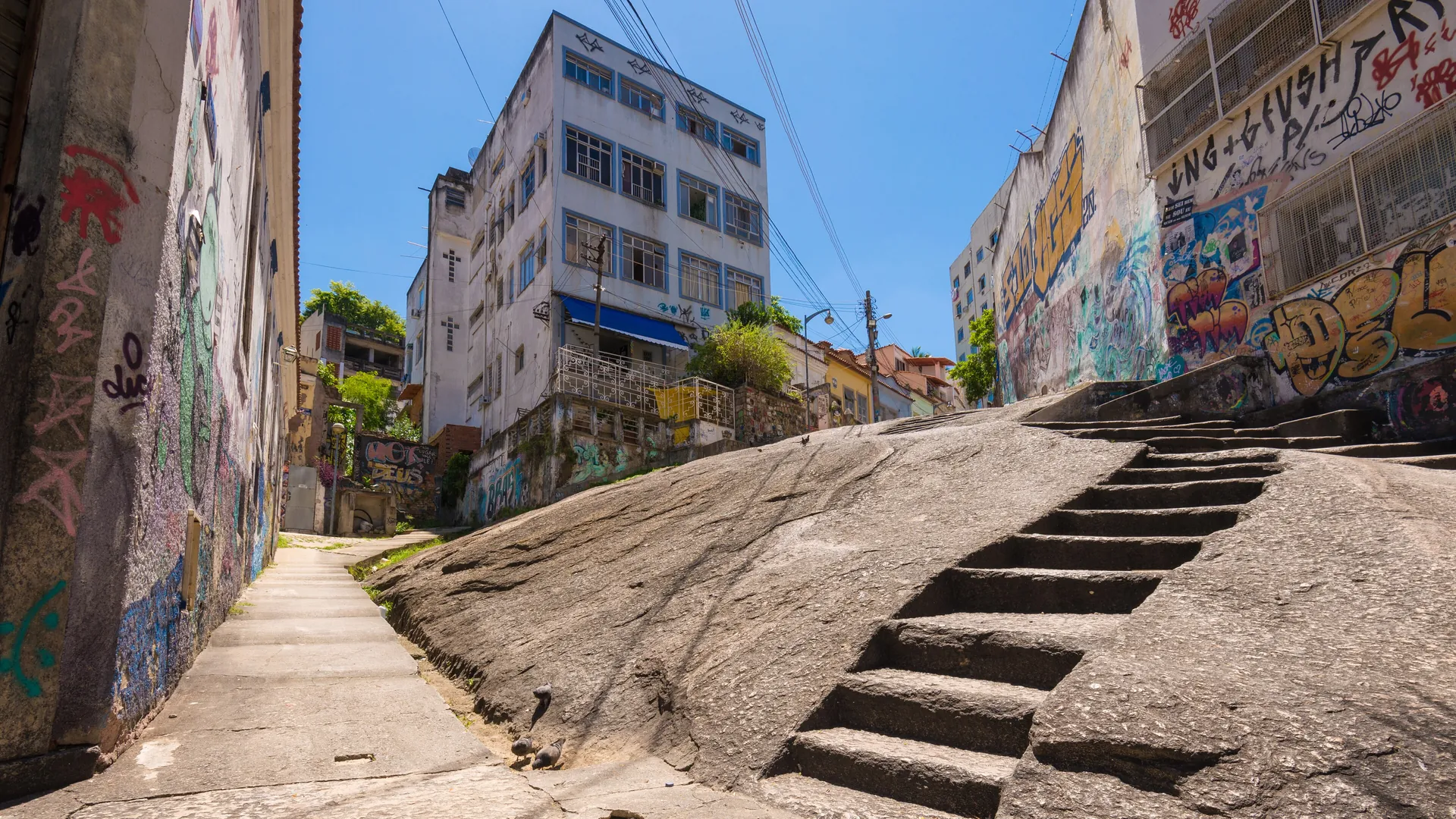 Los escalones de granito tallado de Pedra do Sal ascienden por una roca inclinada entre muros pintados y edificios de apartamentos bajo un cielo azul despejado